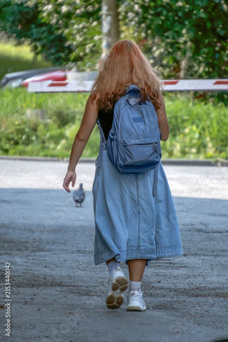 A buxom-haired woman with a backpack walks along the sidewalk on a summer day