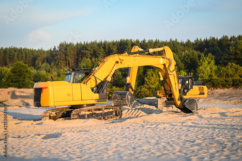 Excavator working in a sandy quarry, digging and moving sand. Industrial construction scene showing heavy machinery operating at a sand extraction site.