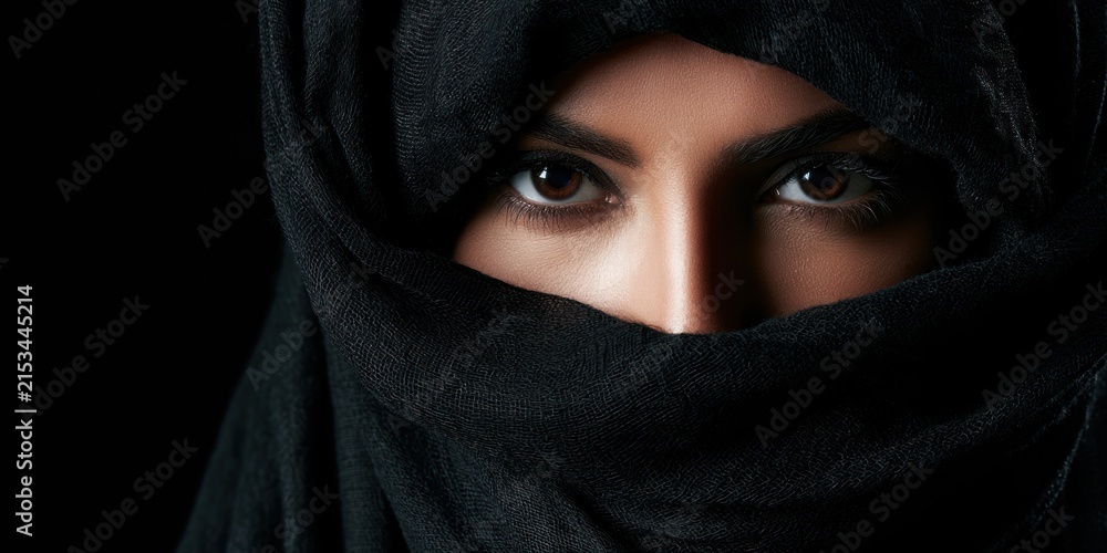 Naklejka premium Womans eyes visible behind black headscarf dramatic portrait on dark background