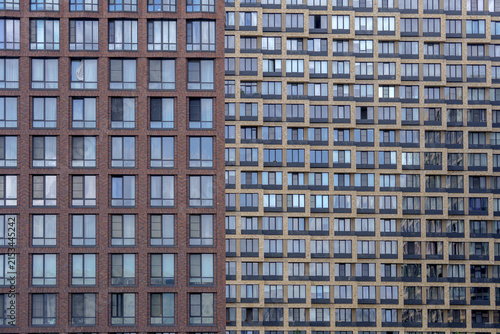 Two contrasting skyscraper facades dividing the frame vertically into brown and yellow brick patterns. Symmetrical window grid layout for minimalistic urban architecture backdrop.