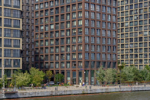 Modern residential skyscrapers on the river embankment as an urban landscape. Highrise apartment buildings with windows and green trees.