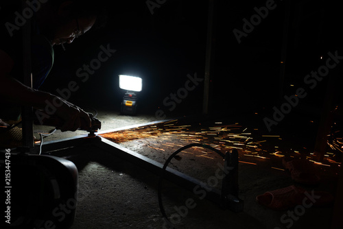 Metalworker using angle grinder on steel bar creating dramatic shower of bright orange sparks at night workshop