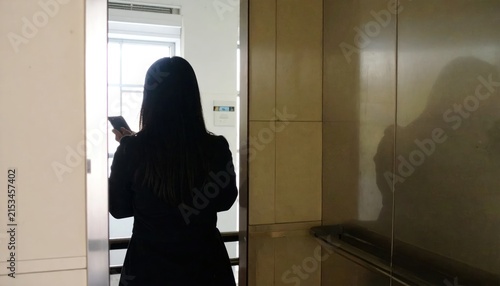 Woman using smartphone while waiting for elevator in office building.