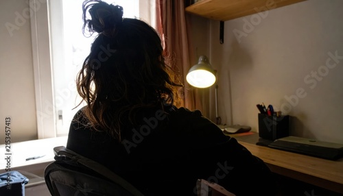 Woman sitting at desk near window during sunset.