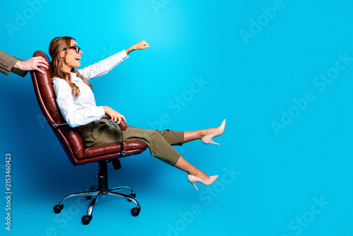 Konstfotografi Young businesswoman celebrating success while being pushed on an office chair by