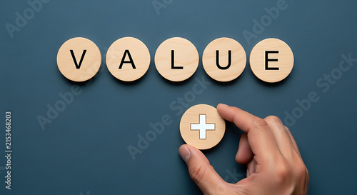 Hand holding wooden value token with plus sign on dark slate background for business growth concept