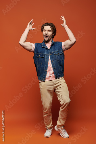 Canvastavla Stylish man expresses joy in vibrant pose against warm orange backdrop