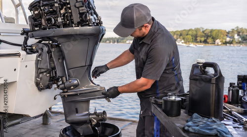Man in cap and gloves servicing a boat engine on the water, draining oil into a bucket. Marine maintenance, boat repair, engine service, waterside work, change oil