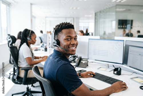 Smiling Black customer service agent wearing headset working at desk in modern call center