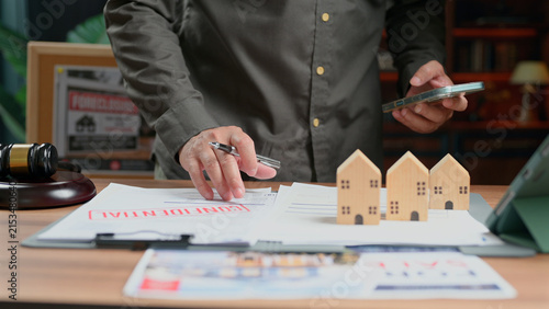 Принти на полотні Person inspects confidential real estate contract documents wooden house models desk office legal dispute property ownership transaction auction gavel negotiator mortgage loan agreement business