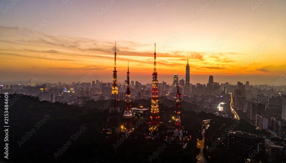 Fototapeta premium Illuminated Telecommunication Towers Stand Tall Over Taipei City Skyline at Sunset with Golden Hour Glow