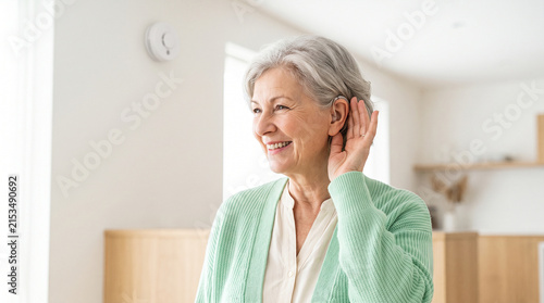 Happy senior woman adjusting hearing aid at home for better hearing and independent living
