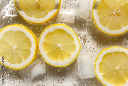 Rondelles de citrons jaunes en gros plan dans de l'eau pétillante avec des glaçons, reflets blancs lumineux