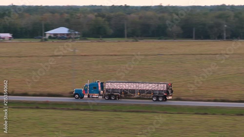 Rural highway traffic with semi truck transporting freight at fast speed, setting sun illuminating road ahead. Safety, supply chain and cargo movement concept.