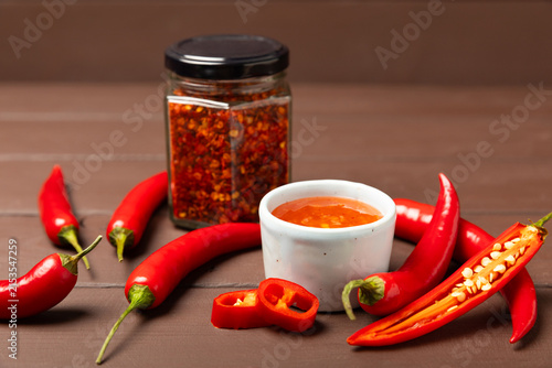 Foto Hot chili sauce  in a bowl with fresh red peppers and chili flakes on wooden cutting board