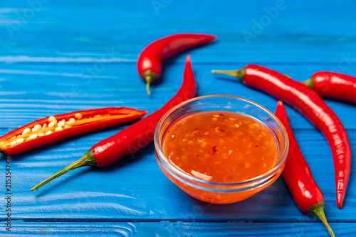 Canvastavla Hot chili sauce  in a bowl with fresh red peppers and chili flakes on wooden cutting board
