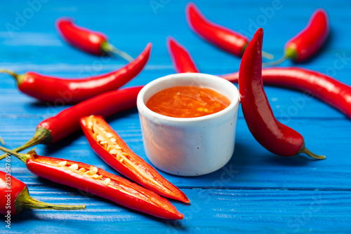 Foto Hot chili sauce  in a bowl with fresh red peppers and chili flakes on wooden cutting board