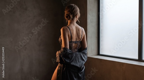 Sensual woman in black lace lingerie and silk robe near window