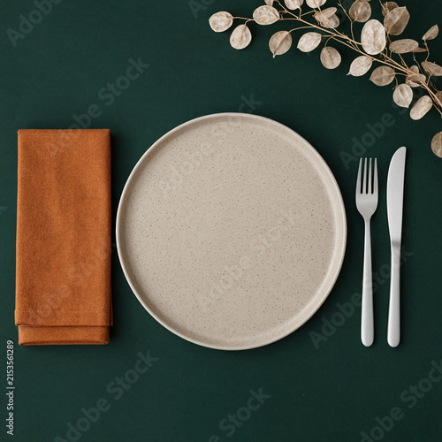 Minimalist place setting with beige plate, orange napkin and cutlery
