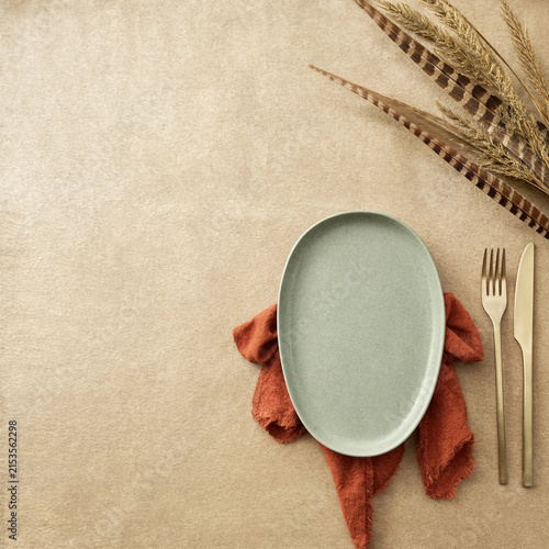 Minimalist table setting with oval plate, rust napkin and feathers