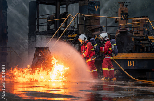 Firefighter Team Battling an Industrial Fire with a Hose while Wearing Full Protective Uniforms, Face Masks, Helmets, and Air Tanks