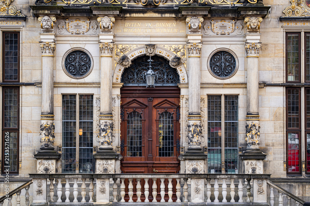 Fototapeta premium Facade with ornate stone columns and sculptures. Facade around an antique wooden entrance. Historic building facade with gilded architectural details. European architecture with facade.