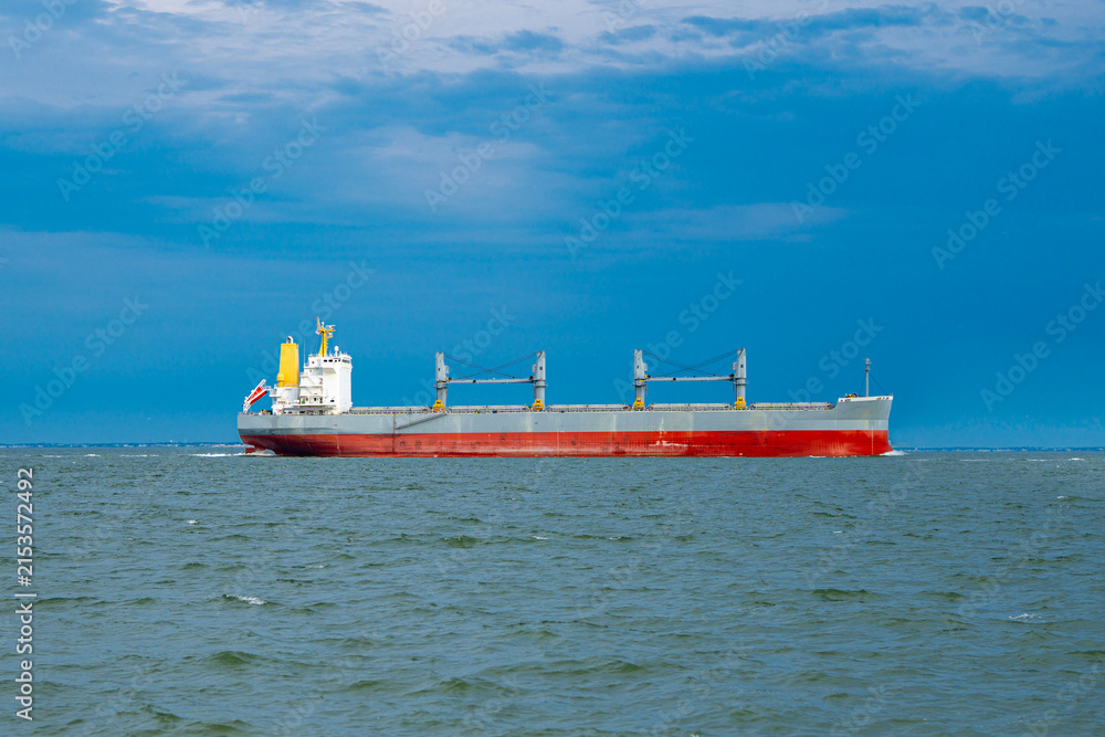 Fototapeta premium Cargo ship sails through coastal waters. Cargo ship carries international sea freight. Large cargo ship serves global logistics. Commercial cargo ship drives worldwide trade.