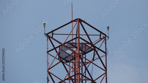 Red Metal Lattice Telecommunication Tower with Lightning Rod and Warning Lights against Blue Sky