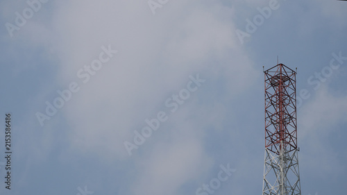 Fotografía Telecommunication tower with red and white patterns against a cloudy blue sky ba