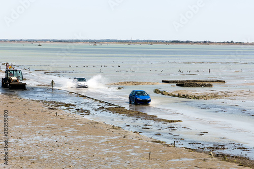 Véhicules roulant sur une route presque recouverte par la mer, engagés sur le passage à marée descendante. Le Gois, île de Noirmoutier.