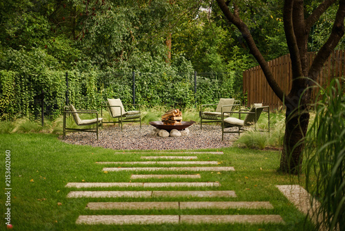 Cozy gravel fire lounge area surrounded by green lawn with a stone pathway in backyard.