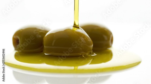 Golden olive oil pouring over fresh green olives on a white plate