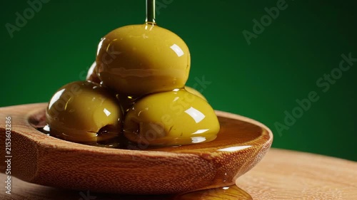 Pouring golden olive oil over fresh green olives in a wooden bowl on rustic table
