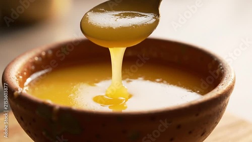 Close-up of a wooden spoon dipping into a bowl of golden clarified butter ghee