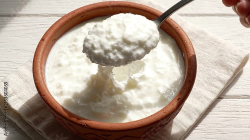 Hand scooping creamy white yogurt from a rustic ceramic bowl on a wooden surface