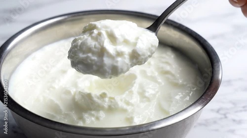 Close-up of a spoon scooping creamy white yogurt from a metal bowl on marble