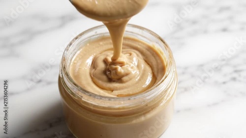 Creamy tahini sauce dripping into a glass jar on a marble surface