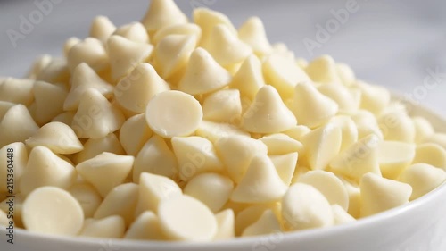 Close up of a pile of creamy white chocolate chips in a white bowl on marble surface