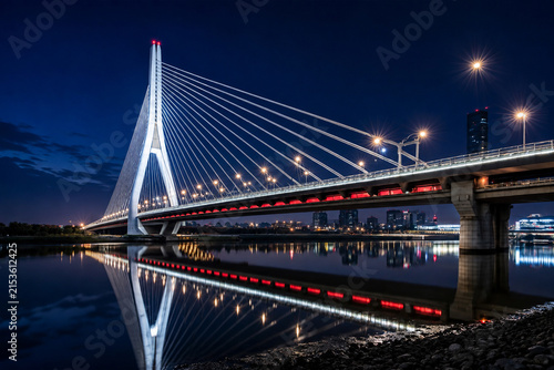Modern illuminated cable stayed bridge over calm water at nighttime