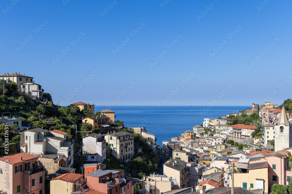 Naklejka premium Riomaggiore on the northwest Mediterranean coast of Italy highlights village valley aligned with sea horizon in bright morning sunlight.