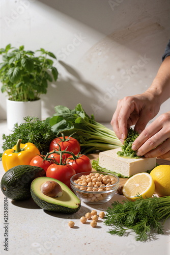 A man chops fresh green herbs on a white kitchen counter, surrounded by various fresh ingredients.