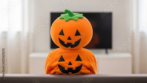 Person wearing a pumpkin head mask and costume watching television at home