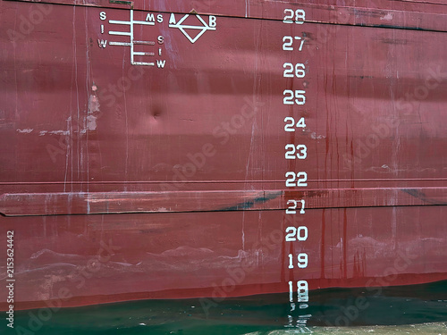 A ship's hull displays draft markings and measuring indicators that highlight its waterline and provide a sense of scale