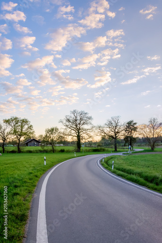 Empty winding road through green countryside at sunset