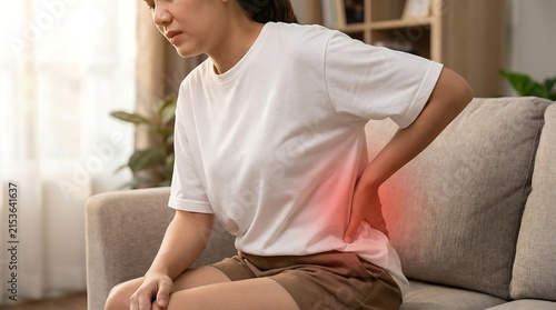 Young woman suffering from back pain while sitting on the sofa at home