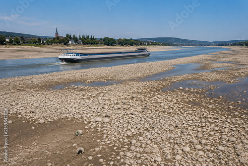 Frachtschiff auf dem Rhein bei extremem Niedrigwasser mit weitläufigen freiliegenden Kiesbänken und ausgetrocknetem Flussbett. Symbolbild für Dürre, Wasserknappheit, Klimawandel sowie die Folgen niedr