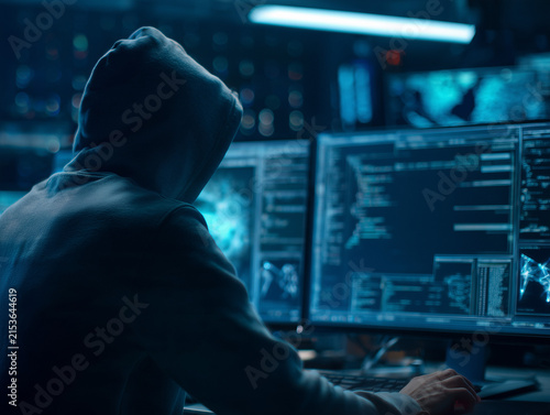 Hacker in hoodie working on computer in dark room