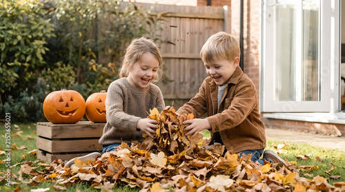 Children playing with dry autumn leaves in a backyard decorated with Halloween pumpkins.