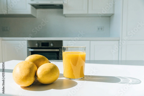 Fresh yellow mangos and glass of mango smoothie on the white table in the white modern kitchen. Copy space
