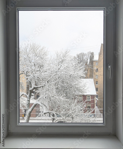 Winter city view from the window with snowy trees and buildings
